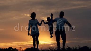 幸福的一家人在日落时在田野里奔跑。 夏夜一家人的剪影。 爱家庭的概念